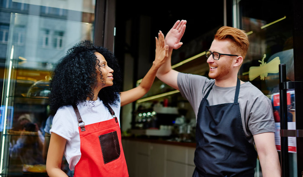 African American woman and Caucasian male waiters high five each other
